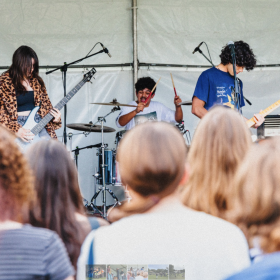 Three young musicians on a stage with crowd in foreground